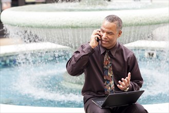 African American businessman talking on cell phone at fountain