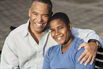 African American father and son hugging on bench