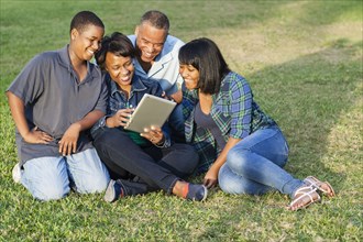 African American family using digital tablet on grass