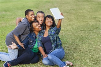 African American family taking selfie with digital tablet on grass