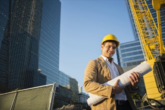 Mixed race architect holding blueprints at construction site