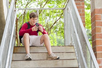 Caucasian teenage boy using cell phone on steps