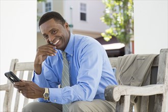 Black businessman using cell phone on bench
