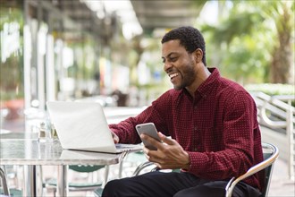 Black businessman using laptop and cell phone in cafe