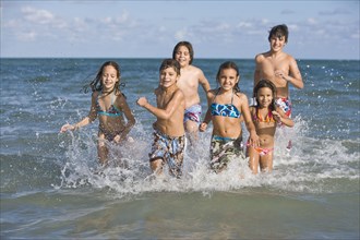 Hispanic children running through ocean surf