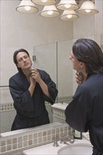 Hispanic man shaving in bathroom mirror