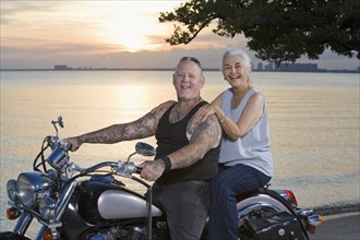 Mother and tattooed son riding motorcycle at the beach