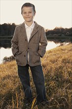 Cute boy in jacket standing near lake
