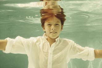 Boy in shirt swimming underwater in swimming pool