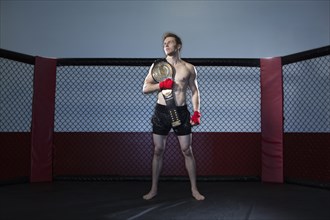 Caucasian cage fighter holding championship belt