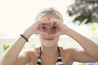 Caucasian girl making heart shape around eyes