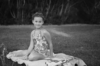 Caucasian girl sitting on towel in backyard