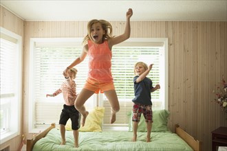 Caucasian children jumping on bed