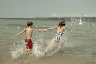Caucasian children splashing together into lake
