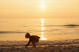 Caucasian boy playing on rocky beach at sunset