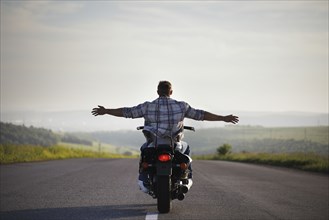 Caucasian man riding motorcycle with arms outstretched