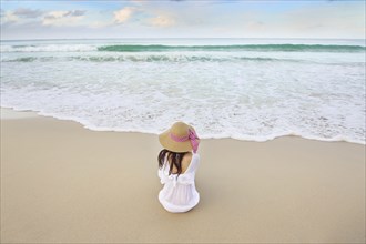 Woman sitting on beach near ocean waves