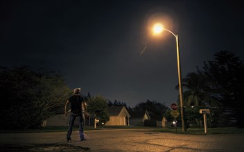 Caucasian man looking up at street light in suburb at night
