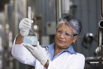 African scientist examining beaker of liquid in factory