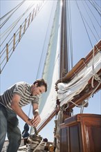Caucasian man hoisting sail on sailboat