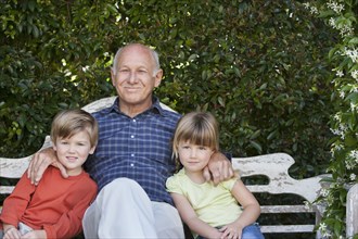 Grandfather sitting with grandchildren on garden bench