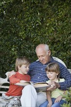 Grandfather reading to grandchildren on garden bench