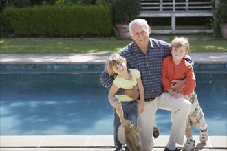 Senior Caucasian man hugging grandchildren by pool