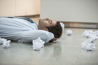 Businessman on floor surrounded by crumpled paper