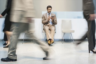 Businessman using cell phone in busy lobby area