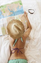 Woman in bikini reading map on bed