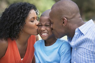 African American parents kissing son's cheeks