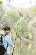 Asian boy carrying fishing pole by lake