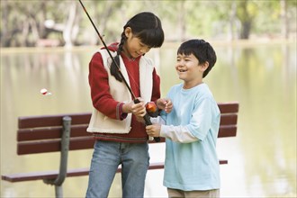 Children threading fishing pole by lake