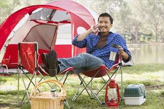 Asian man relaxing in lawn chair at campsite