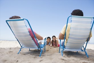 Parents watching children from lawn chairs on beach