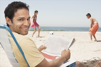 Hispanic father relaxing as children play on beach
