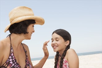 Mother rubbing sunscreen on daughter on beach