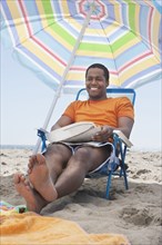 Mixed race man sitting in lawn chair on beach