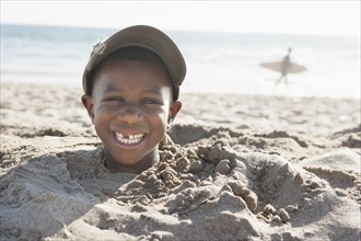 Smiling boy buried in sand on beach