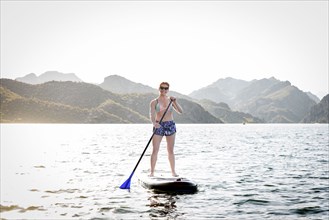 Caucasian woman standing on paddleboard in river