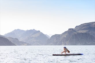 Caucasian woman stretching on paddleboard in river