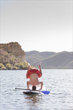 Hispanic man doing headstand on paddleboard in river