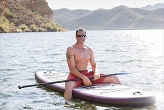 Hispanic man sitting on paddleboard in river