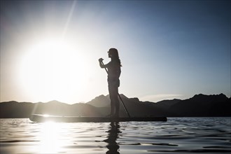 Silhouette of Caucasian woman standing on paddleboard in river