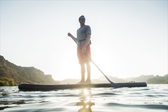 Smiling Hispanic man standing on paddleboard in river