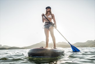 Hispanic woman standing on paddleboard in river