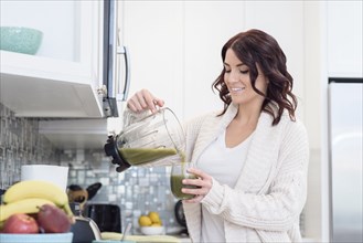 Caucasian woman pouring green juice smoothie in domestic kitchen