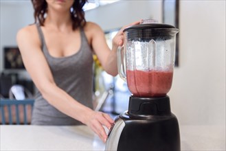 Caucasian woman mixing fruit smoothie in blender