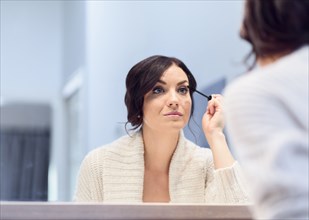 Caucasian woman applying mascara in mirror