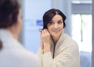 Caucasian woman fastening earring in mirror